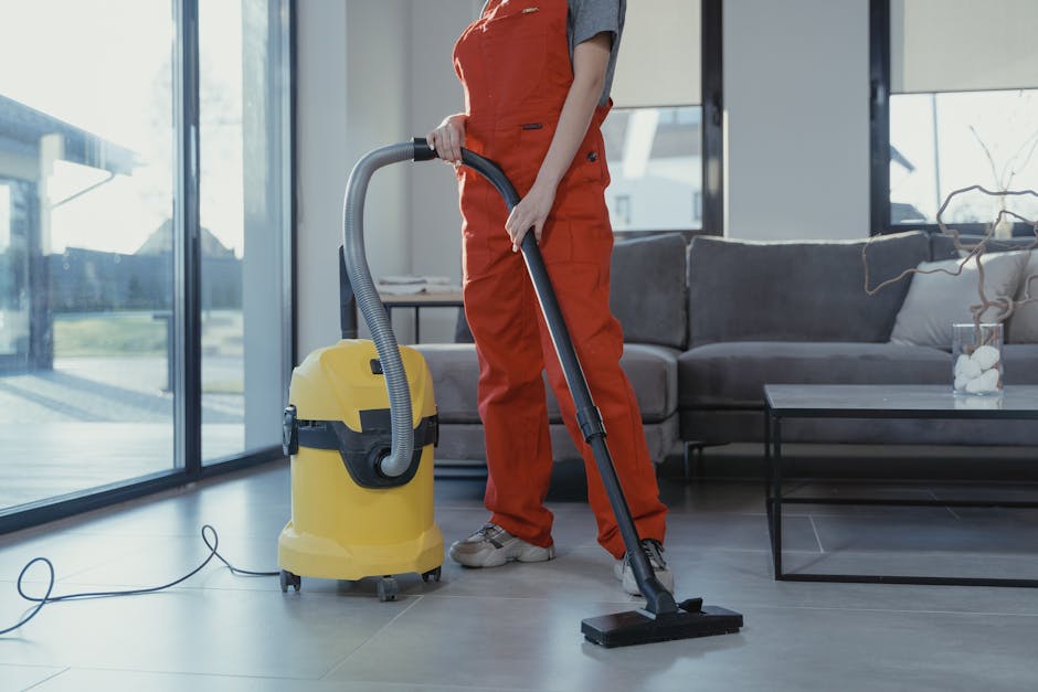 Professional cleaner in red coveralls vacuuming a modern living room